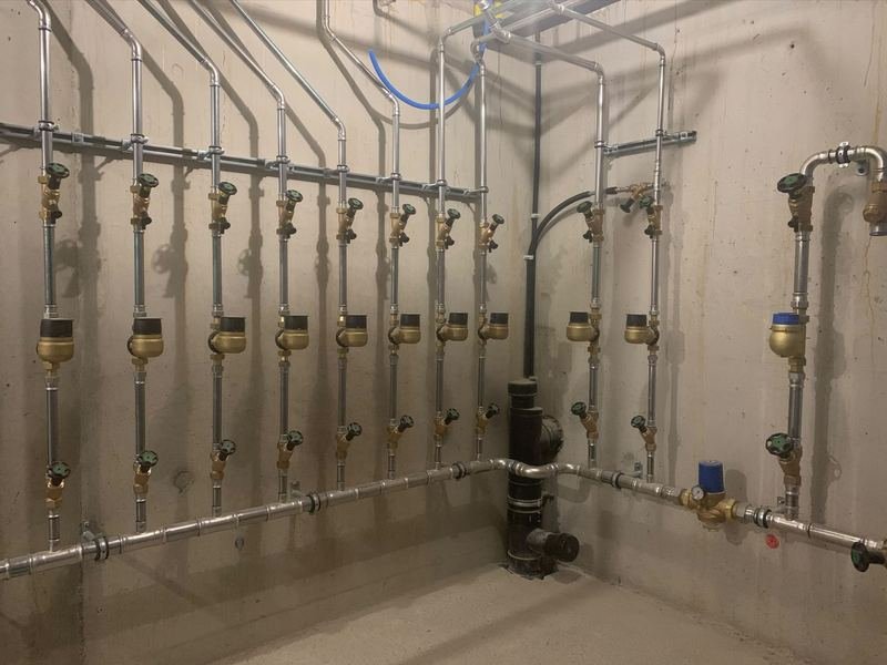 Local de distribution d'eau d'un immeuble : une colonne par logement avec compteur et deux vannes, conduite principale en inox et réducteur de pression.
