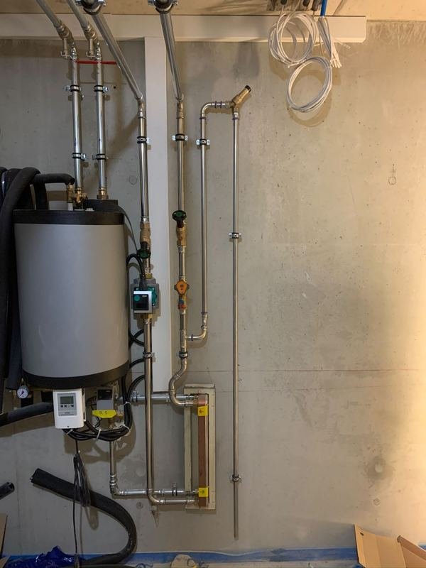 Local technique : chauffe-eau, pompe de circulation, échangeur à plaques et régulation, raccordés par des conduites en inox serties et fixées au mur.