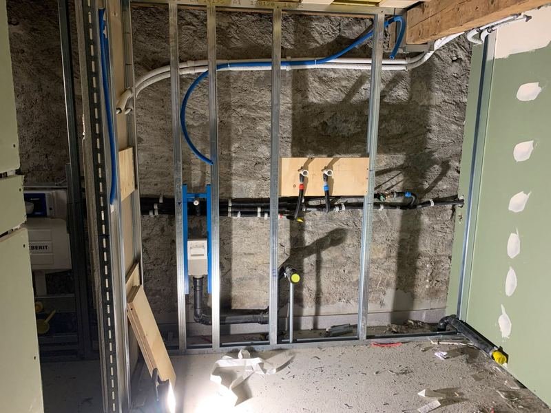 Salle de bains en cours d'installation, cloisons ouvertes : ossature métallique, bâtis-supports Geberit, conduites d'eau chaude et froide, évacuations noires.