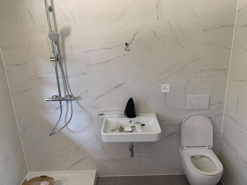 Salle de douche en fin de chantier : colonne de douche thermostatique, lavabo suspendu et WC suspendu, carrelage effet marbre.